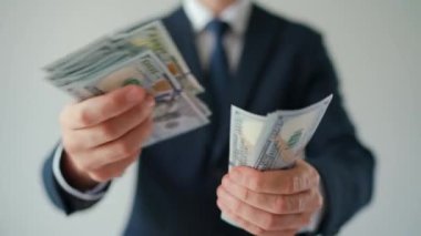 Resmi olarak giyinmiş bir adam Amerikan dolarlarını sayıyor, yakın plan. Ağır çekim. Yatırım, başarı, finansal beklentiler veya kariyer ilerlemesi kavramı.