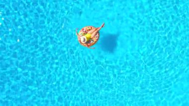 Top down view of a woman in yellow swimsuit lying on a donut in the pool. Concept of summer lifestyle, rest and relaxation