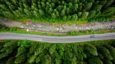 Top down view of cars driving along the road in the mountains among the coniferous forest