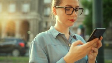 Gün batımında dışarıda dikilirken akıllı telefon kullanan bir kadın. İletişim, iş günü, yoğun yaşam konsepti. Yavaş çekim