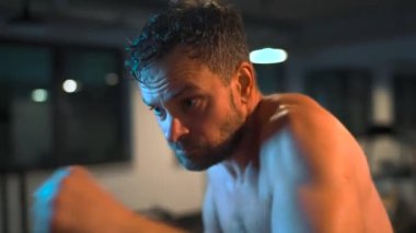 Alone male boxer is working out blows on a punching bag in a gym in evening. Slow motion