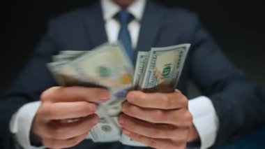 Resmi olarak giyinmiş bir adam Amerikan dolarlarını sayıyor, yakın plan. Yatırım, başarı, finansal beklentiler veya kariyer ilerlemesi kavramı.