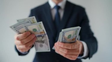 Resmi olarak giyinmiş bir adam Amerikan dolarlarını sayıyor, yakın plan. Ağır çekim. Yatırım, başarı, finansal beklentiler veya kariyer ilerlemesi kavramı.