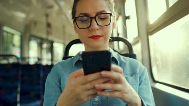 公共交通 坐在电车里戴眼镜的女人用智能手机和朋友聊天和发短信 慢动作 — 图库视频影像