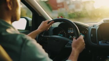 Adam yol boyunca araba sürüyor, batan güneş ön camda parlıyor. Sürücülerin omzunun arkasından bak.