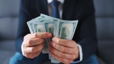 Resmi olarak giyinmiş bir adam Amerikan dolarlarını sayıyor, yakın plan. Yatırım, başarı, finansal beklentiler veya kariyer ilerlemesi kavramı.