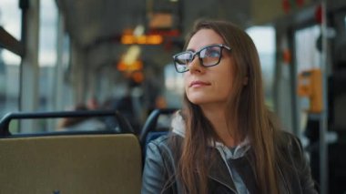 Public transport. Woman in glasses in tram using smartphone chatting and texting with friends, slow motion. City, urban, transportation.