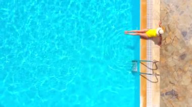 Sarı mayolu ve şapkalı bir kadın havuzun kenarında oturuyordu. Yaz yaşam tarzı, dinlenme ve rahatlama kavramı