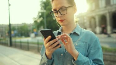 Woman using smartphone while standing outdoors at sunset. Communication, work day, busy life concept.