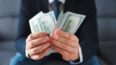 Resmi olarak giyinmiş bir adam Amerikan dolarlarını sayıyor, yakın plan. Yatırım, başarı, finansal beklentiler veya kariyer ilerlemesi kavramı.