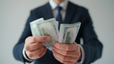 Resmi olarak giyinmiş bir adam Amerikan dolarlarını sayıyor, yakın plan. Ağır çekim. Yatırım, başarı, finansal beklentiler veya kariyer ilerlemesi kavramı.