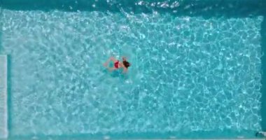 Top down view of a woman in red swimsuit swimming in the pool, slow motion. Camera descends over the pool. Summer lifestyle