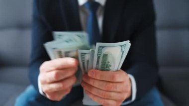 Resmi olarak giyinmiş bir adam Amerikan dolarlarını sayıyor, yakın plan. Yatırım, başarı, finansal beklentiler veya kariyer ilerlemesi kavramı.