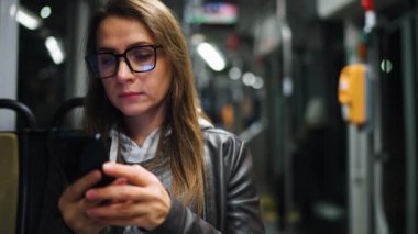 Geceleri toplu taşıma. Tramvaydaki gözlüklü kadın akıllı telefon konuşmaları yapıyor ve arkadaşlarıyla mesajlaşıyor. Şehir, şehir, ulaşım.