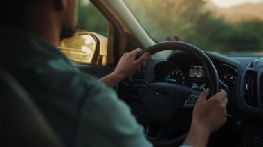 Adam yol boyunca araba sürüyor, batan güneş ön camda parlıyor. Sürücülerin omzunun arkasından bak.