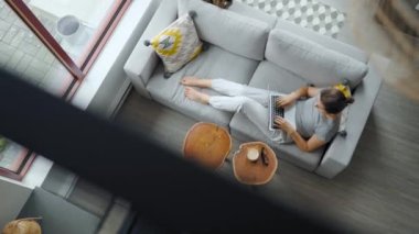 Overhead shot of woman using laptop with green mock-up screen, lying on couch at home