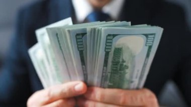 Resmi olarak giyinmiş bir adam Amerikan dolarlarını sayıyor, yakın plan. Yatırım, başarı, finansal beklentiler veya kariyer ilerlemesi kavramı.