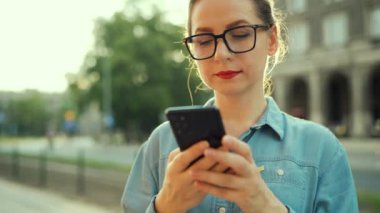 Gün batımında dışarıda dikilirken akıllı telefon kullanan bir kadın. İletişim, iş günü, yoğun yaşam konsepti. Yavaş çekim