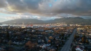Aerial hyperlapse of a residential suburban district and cargo terminal with cargo ships in Vancouver, BC, Canada. Sunset with rainy cloudy sky.