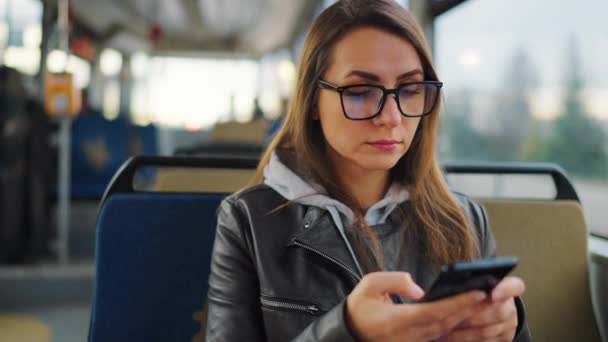 公共交通機関だ スマートフォンのチャットや友人とのテキストメッセージを使用してトラムのメガネの女性 スローモーション — ストック動画