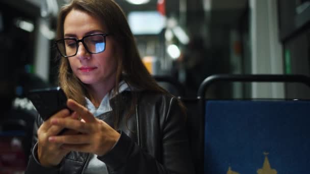 公共交通工具在夜间 坐在电车里戴眼镜的女人用智能手机和朋友聊天和发短信 — 图库视频影像