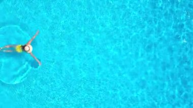 Top down view of a woman in yellow swimsuit and hat swimming in the pool. Summer lifestyle