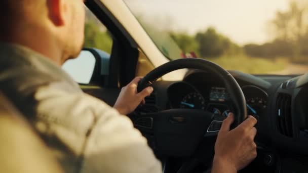 男は道路に沿って車を運転し 夕日がフロントガラスに輝いています ドライバーの肩の後ろからの眺め — ストック動画
