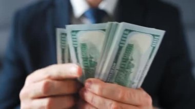 Resmi olarak giyinmiş bir adam Amerikan dolarlarını sayıyor, yakın plan. Yatırım, başarı, finansal beklentiler veya kariyer ilerlemesi kavramı.