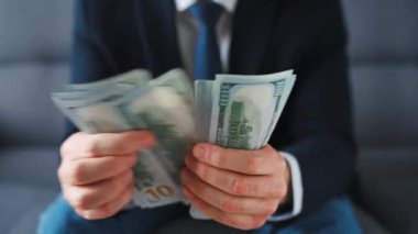 Resmi olarak giyinmiş bir adam Amerikan dolarlarını sayıyor, yakın plan. Yatırım, başarı, finansal beklentiler veya kariyer ilerlemesi kavramı.