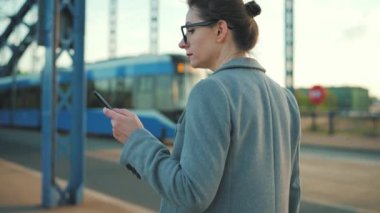 Sabahın erken saatlerinde şehirde dolaşan ve akıllı telefon kullanan beyaz bir iş kadını. İletişim, iş günü, yoğun yaşam konsepti. Yavaş çekim