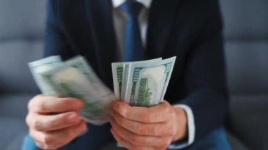 Resmi olarak giyinmiş bir adam Amerikan dolarlarını sayıyor, yakın plan. Yatırım, başarı, finansal beklentiler veya kariyer ilerlemesi kavramı.