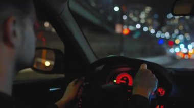 Gece şehrinin sokaklarında araba süren bir adam. Arabanın camında bir parlama var. Arabanın arka koltuğundan bak..
