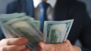 Resmi olarak giyinmiş bir adam Amerikan dolarlarını sayıyor, yakın plan. Yatırım, başarı, finansal beklentiler veya kariyer ilerlemesi kavramı.