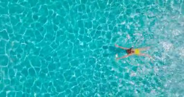 Top down view of a woman in yellow swimsuit swimming in the pool. Summer lifestyle