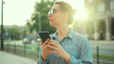 Gün batımında dışarıda dikilirken akıllı telefon kullanan bir kadın. İletişim, iş günü, yoğun yaşam konsepti. Yavaş çekim
