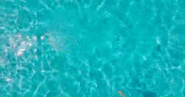 Sarı mayo giymiş bir kadının havuzda sırt üstü yatışı. Rahatlatıcı konsept, yaz yaşam tarzı. Kamera havuzun üzerinde yükseliyor.