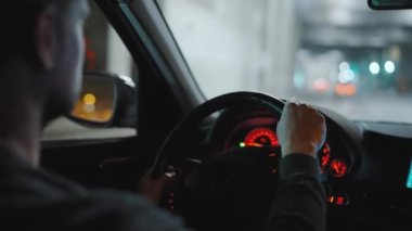 Gece şehrinin sokaklarında araba süren bir adam. Arabanın camında bir parlama var. Arabanın arka koltuğundan bak..