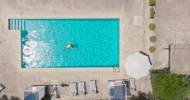 Top down view of a woman in an yellow swimsuit lying on her back in the pool. Relaxing concept, summer lifestyle