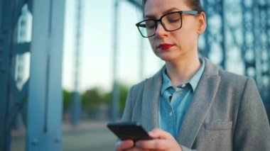 Sabahın erken saatlerinde şehirde dolaşan ve akıllı telefon kullanan beyaz bir iş kadını. İletişim, iş günü, yoğun yaşam konsepti. Yavaş çekim