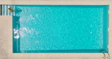 Top down view of a woman in yellow swimsuit swimming in the pool. Summer lifestyle