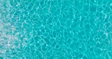 Yüzme havuzundaki saf mavi suyun yüzeyinde hafif yansımalar, ağır çekim. Hava görüntüleri