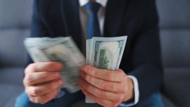 Resmi olarak giyinmiş bir adam Amerikan dolarlarını sayıyor, yakın plan. Yatırım, başarı, finansal beklentiler veya kariyer ilerlemesi kavramı.