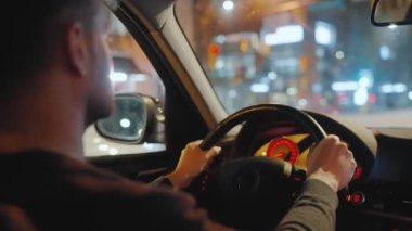 Gece şehrinin sokaklarında araba süren bir adam. Arabanın camında bir parlama var. Arabanın arka koltuğundan bak..