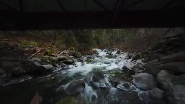 Büyük taşların arasında akan ve kıyılarda ağaçlarla çevrili bir dağ nehrinin üzerinden hızlı bir uçuş. Chilliwack, British Columbia, Kanada. POV FPV insansız hava aracı ile filme alındı.