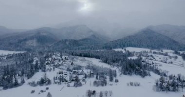 Karla kaplı muhteşem bir dağ manzarası ve vadideki köy üzerinde uçmak. Soğuk ve kasvetli bir günde peri kışı manzarası. Tatra Dağları, Zakopane, Polonya
