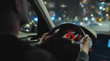 Gece şehrinin sokaklarında araba süren bir adam. Arabanın camında bir parlama var. Arabanın arka koltuğundan bak..