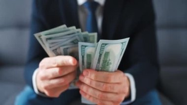 Resmi olarak giyinmiş bir adam Amerikan dolarlarını sayıyor, yakın plan. Yatırım, başarı, finansal beklentiler veya kariyer ilerlemesi kavramı.