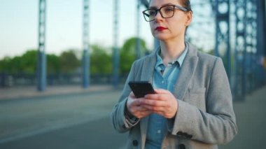 Caucasian businesswoman in a coat walking around the city in the early morning and using smartphone, slow motion. Communication, work day, busy life concept.