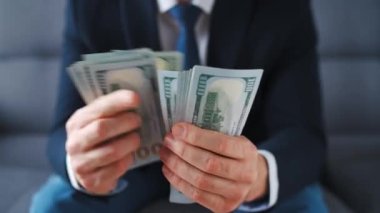 Resmi olarak giyinmiş bir adam Amerikan dolarlarını sayıyor, yakın plan. Yatırım, başarı, finansal beklentiler veya kariyer ilerlemesi kavramı.