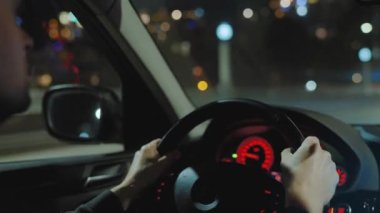 Gece şehrinin sokaklarında araba süren bir adam. Arabanın camında bir parlama var. Arabanın arka koltuğundan bak..